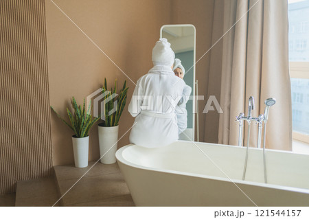 Mature adult old woman looking at mirror applying nourishing anti age face cream doing daily beauty routine. Senior woman with white mask creme on skin gets facial treatment Skin care aging skincare Mature adult old woman looking at mirror applying nourishing anti age face cream doing daily beauty routine. Senior woman with white mask creme on skin gets facial treatment Skin care aging skincare 121544157
