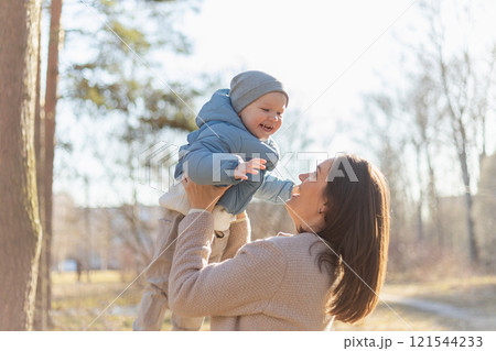 Happy family outdoor. Mother embracing her child outdoor. Mom lifting in air little toddler child son. Woman and little baby boy resting walking in park. Mother hugs baby with love care 121544233