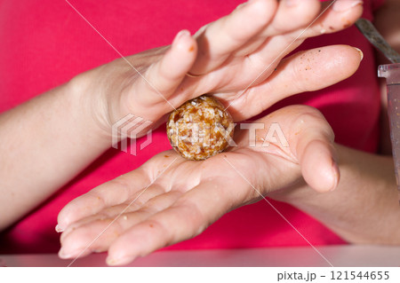 Woman makes candies from dried fruits. From prunes, dates and coconut. Rolls the ball in the palms. 121544655