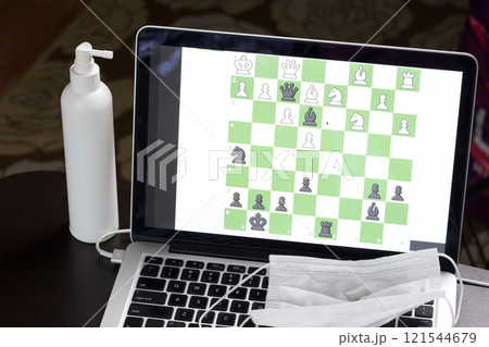 Chess task on laptop screen online. Near antibacterial spray and medical mask. Leisure in self-isolation. International chess day. Chess task on laptop screen online. Near antibacterial spray and medical mask. Leisure in self-isolation. International chess day. 121544679