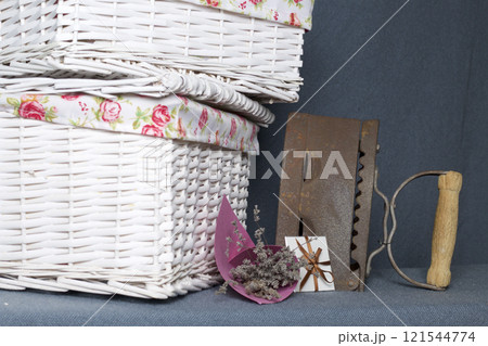 Old iron, heated by hot coals. Located on gray fabric. Nearby are wicker baskets, a bouquet of dried flowers and a greeting card. 121544774