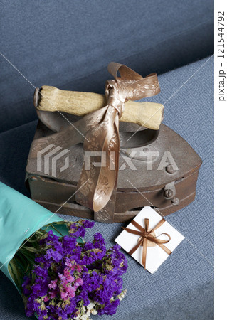 Old iron, heated by hot coals. Located on gray fabric. Nearby are bouquet of dried flowers and a greeting card. Old iron, heated by hot coals. Located on gray fabric. Nearby are bouquet of dried flowers and a greeting card. 121544792