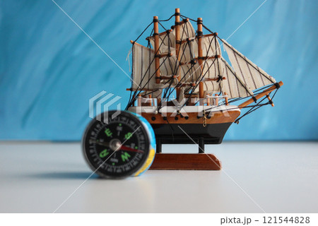 Wooden Sailing Ship Model And Vintage Compass On White Surface Over Blue Backdrop 121544828
