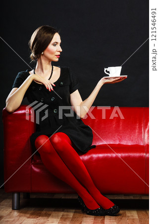 Retro woman holds tea cup sitting on sofa Retro woman holds tea cup sitting on sofa 121546491