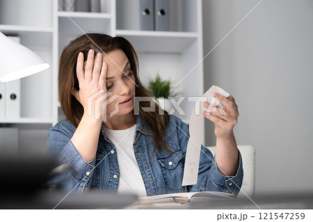 A stressed woman in her messy home office reviews financial receipts, battling anxiety as she reflects on her ongoing financial difficulties and daily challenges that overwhelm her A stressed woman in her messy home office reviews financial receipts, battling anxiety as she reflects on her ongoing financial difficulties and daily challenges that overwhelm her 121547259