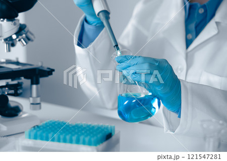 A skilled laboratory technician is engaged in their work utilizing a pipette while wearing blue gloves, showcasing precision and adherence to safety protocols in a scientific research environment 121547281