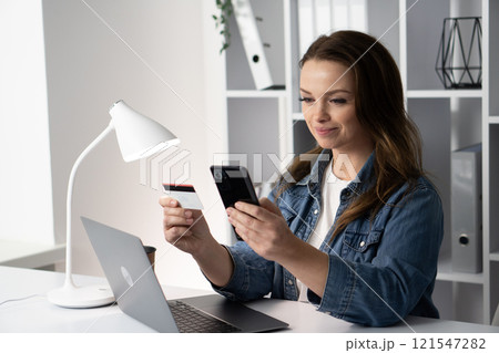 A young professional is actively engaged in online shopping, utilizing a credit card and a smartphone to make purchases, showcasing a convenient modern lifestyle where technology meets commerce 121547282