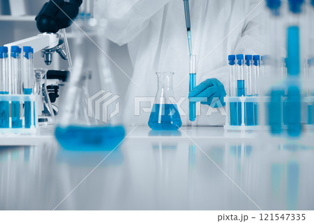 A dedicated scientist conducts experiments with blue solutions, demonstrating precision and innovation in biochemistry, microbiology, and healthcare, using beakers and flasks for safety 121547335