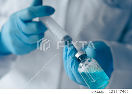 A skilled Laboratory Technician methodically preparing a precise dosage using a syringe and a vial containing a striking blue liquid, indicative of thorough biomedical research and testing 121547403