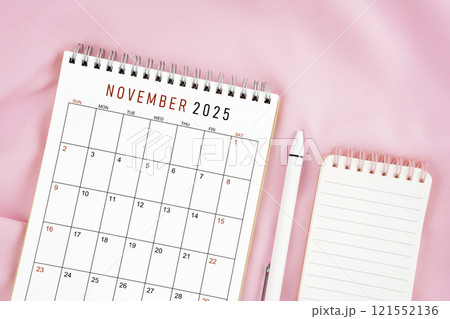 November 2025 month calendar and pen with open diary on pink fabric background. 121552136