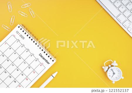 December 2025, Monthly desk calendar for 2025 year and alarm clock with paper clips on yellow 121552137