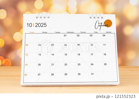 October 2025 desk calendar on wooden table with gold light bokeh background. 121552323