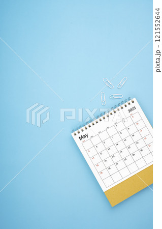 Desk calendar for May 2025 and white paper clip on a light blue background. 121552644