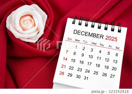 December 2025 desk calendar and pink rose on red textile. 121552818