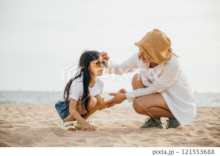 Family fun on the beach at sunset. Mother and daughter sitting playing in the sand. Caribbean vacation vibes with happiness togetherness and joy. A carefree moment of bonding 121553688