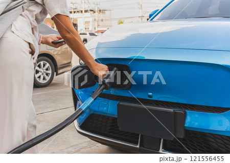 Woman charging at electric vehicle at charging station and paying service in mobile app. 121556455