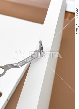 Assembling white furniture with metal wrench and cam lock fastener on brown surface 121556525