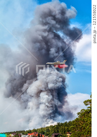 Big amphibious fire aircraft drops water on large forest fire near the village 121558022