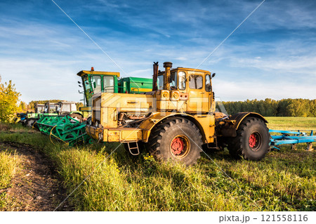 Wheeled tractors and combine harvester standing in a row on an agricultural field 121558116