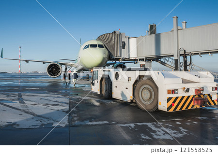 The tow tractor approaches the passenger airplane at the boarding bridge 121558525