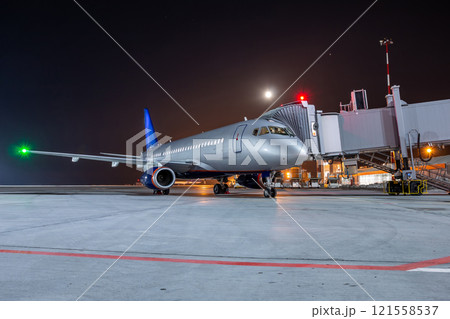 Modern passenger airliner at the jet bridge on night airport apron 121558537