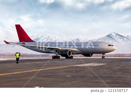 Airport marshaller meets passenger airliner on the background of high picturesque mountains Airport marshaller meets passenger airliner on the background of high picturesque mountains 121558717