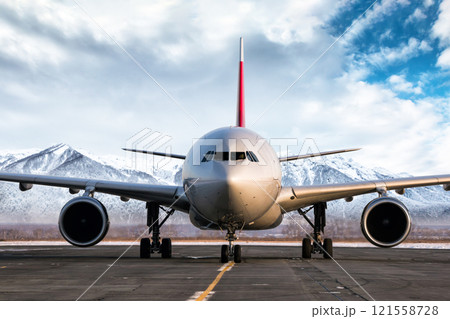 Front view of a wide body passenger aircraft at the airport apron on the background of high picturesque mountains Front view of a wide body passenger aircraft at the airport apron on the background of high picturesque mountains 121558728