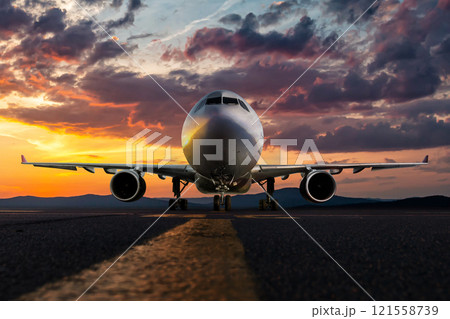 Front view of the wide body passenger aircraft at the airport apron against the backdrop of a scenic sunrise sky 121558739