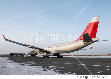 Wide body passenger airplane with boarding stairs at the winter airport apron. Shuttle bus near the aircraft 121558748