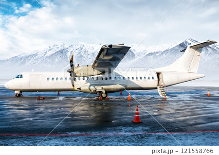 White passenger turboprop airplane on the winter airport apron with an open staircase ladder on the background of high scenic mountains 121558766