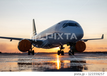 Modern passenger airplane on the airport apron against the backdrop of a picturesque sunset 121559257