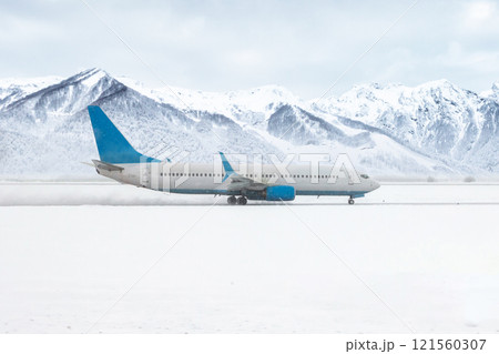 A passenger airliner moves on the runway in a severe snowstorm on the background of high snow capped mountains 121560307