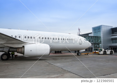 White passenger airplane and tow tractor parked at the terminal on the airport apron 121560501