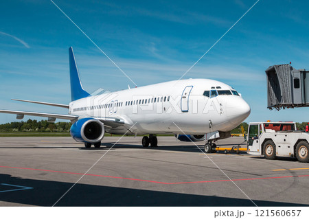 Tow tractor pushes the passenger airplane away from the air bridge 121560657