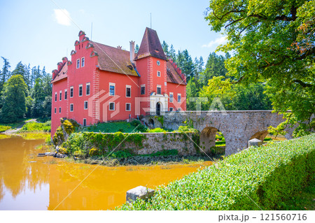 Cervena Lhota Castle majestically rises from a rocky island amidst a tranquil lake in Czechia, surrounded by lush greenery and reflecting bright colors under a clear sky. 121560716