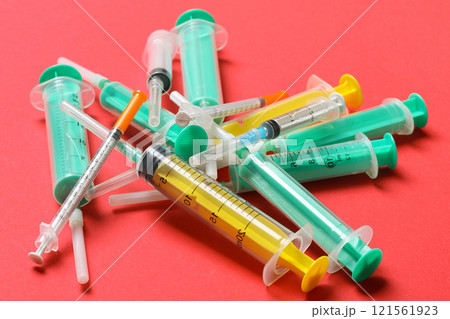 Top view of a pile of medical syringes and insulin syringes with needles at red background with copy space. Injection treatment concept 121561923