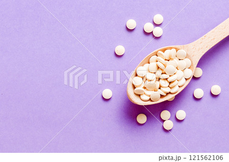 Heap of white pills on colored background. Tablets scattered on a table. Pile of red soft gelatin capsule. Vitamins and dietary supplements concept 121562106