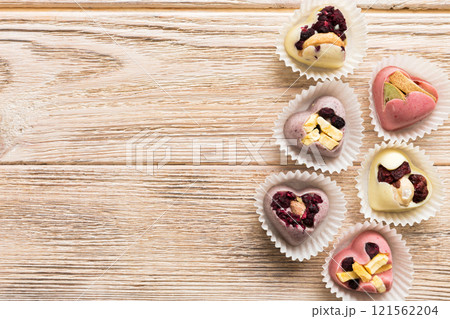 chocolate sweets in the form of a heart with fruits and nuts on a colored background. top view with space for text, holiday concept chocolate sweets in the form of a heart with fruits and nuts on a colored background. top view with space for text, holiday concept 121562204