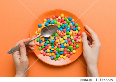 the girl holds cutlery in her hands and eats sweets in a plate. Health and obesity concept, top view on colored background 121562289