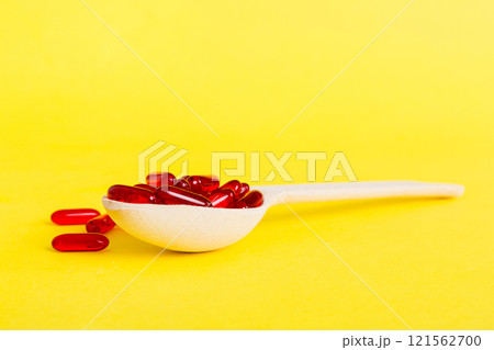 Vitamin capsules in a spoon on a colored background. Pills served as a healthy meal. Red soft gel vitamin supplement capsules on spoon 121562700