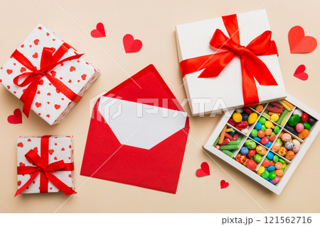 Red envelope with candy and gift box and Valentines hearts on colored background. Flat lay, top view. Romantic love letter for Holiday concept Red envelope with candy and gift box and Valentines hearts on colored background. Flat lay, top view. Romantic love letter for Holiday concept 121562716