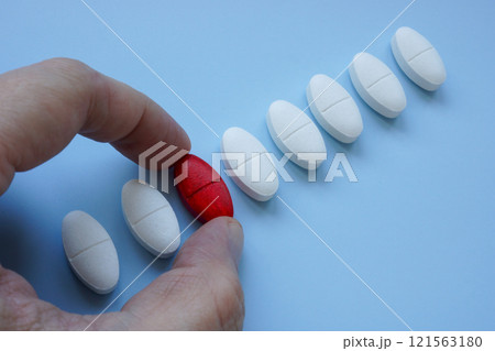 Hand picking a red pill from a row of ordinary ones. Choice and individuality. 121563180