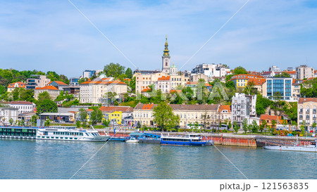 The Sava River flows through Belgrade, showcasing vibrant waterfront buildings and boats docked along the shore under a clear blue sky on a sunny day. 121563835