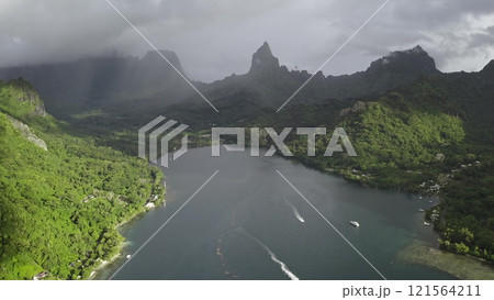 Boats sailing Opunohu bay, green rainforest mountains and volcanic peaks in dramatic rain clouds, Moorea tropical island, French Polynesia. Remote wild nature exotic travel. Aerial view drone panorama Boats sailing Opunohu bay, green rainforest mountains and volcanic peaks in dramatic rain clouds, Moorea tropical island, French Polynesia. Remote wild nature exotic travel. Aerial view drone panorama 121564211