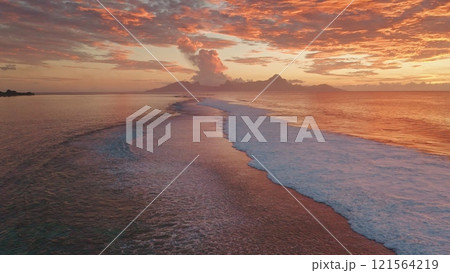 Ocean waves gently rolling sand shore of Tahiti tropical island at sunset. Vibrant orange colors and dramatic clouds reflecting in water. Remote wild nature paradise, exotic summer travel. Aerial shot Ocean waves gently rolling sand shore of Tahiti tropical island at sunset. Vibrant orange colors and dramatic clouds reflecting in water. Remote wild nature paradise, exotic summer travel. Aerial shot 121564219
