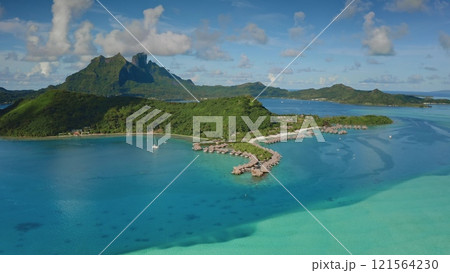 Breathtaking aerial perspective of turquoise coral reef lagoon, overwater bungalows, green forest hills, mount Otemanu forming a mesmerizing tropical oasis in Bora Bora, French Polynesia. Drone flight 121564230