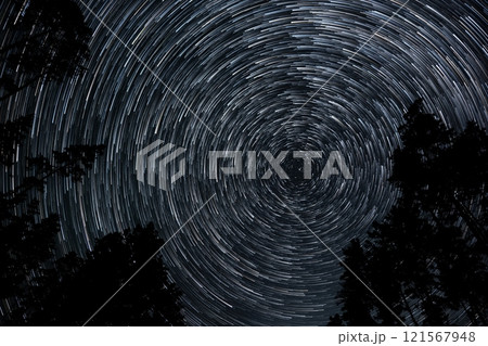Stunning star trails swirl over a dark forest in the night sky 121567948