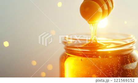 Honey drizzling from dipper into a glass jar on a light backdrop. Liquid honey pouring. Concept of natural sweetness, bee products and gourmet indulgence. Banner. Copy space. 121569152