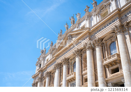The majestic St. Peter's Basilica features grand architecture with towering columns and intricate sculptures under a radiant blue sky, showcasing its historical significance and beauty in Vatican. 121569314