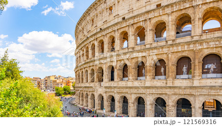 The majestic Colosseum stands prominently under a bright sky in Rome. Visitors admire its architecture, while trees and bustling city life create a vibrant atmosphere. 121569316